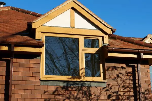 A golden oak flush sash window with double-glazed panels installed on a house with brown brickwork and a pitched roof.